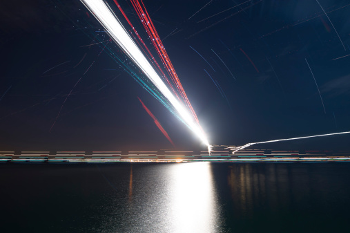 Light trails of airplanes approaching airport during the night, sea as foreground.