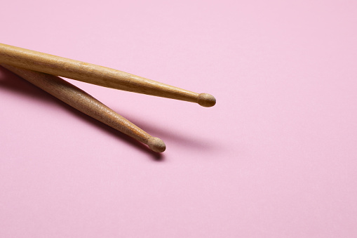 Two wooden drum sticks on pink background, space for text