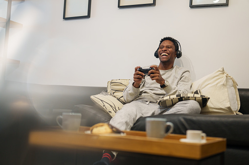 Wide view of African American man laughing holding joystick while playing online games at living room