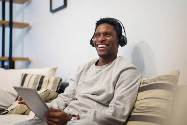 istock Adult African American man sitting on sofa while using digital tablet 1867984643