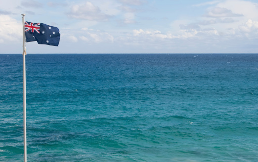 An Australian flag flying over blue sea, near Bondi Beach. Lots of space for copy. Can be flipped horizontally if you want so the flag aligns right, except you get the flag flying the other direction.