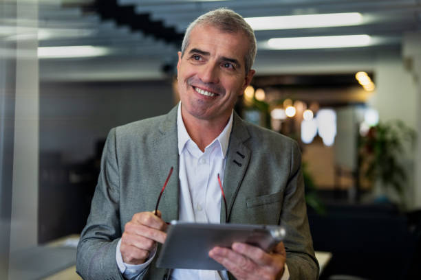 istock Thoughtful senior businessman walking on hallway while holding digital tablet 1867987330