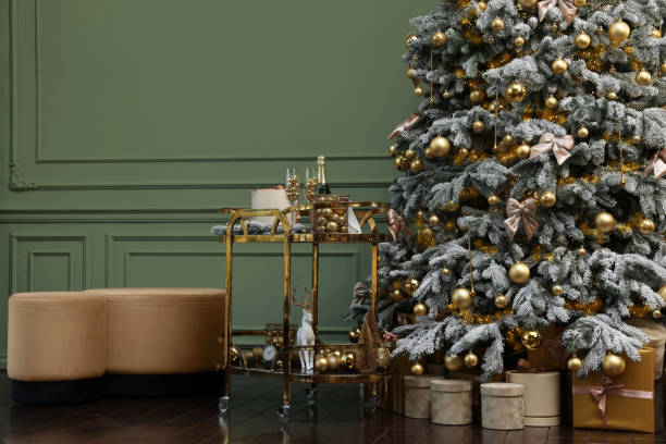 Beautiful Christmas tree, gift boxes, table and festive decor near olive wall indoors. Interior design