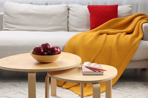 Red apples with book on nesting tables and comfortable sofa in living room. Interior design
