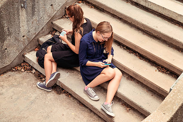 istock Two high school teenagers texting on staircase. 186800908