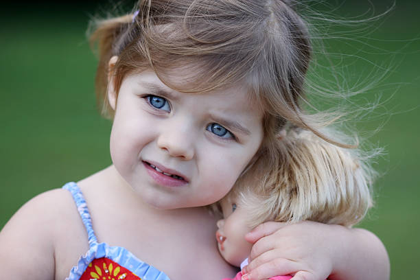 Cute little girl clutching her doll with a worried look on her face. Beautiful blue eyes.