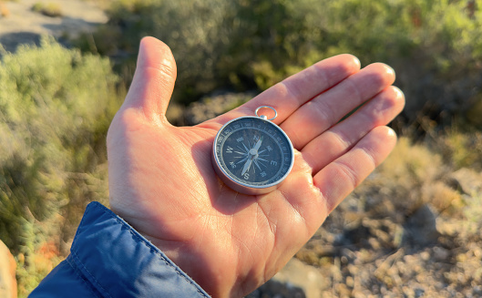 Compass in hand in mountains. Tourist compass for orientation on terrain. Magnetic declination alculator. Map reading and land navigation concept. Orient on maps in mountains