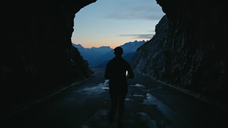 SLO MO Female runner with headlamp and phone jogging out of dark tunnel