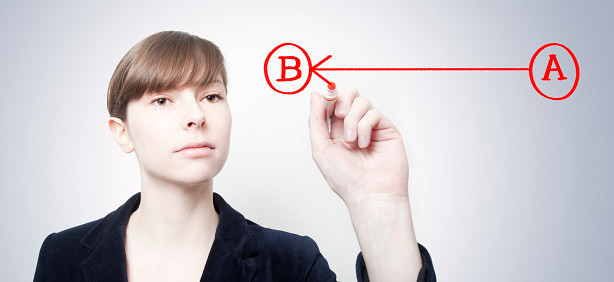 Attractive young Caucasian businesswoman drawing a diagram showing an arrow going from A to B.