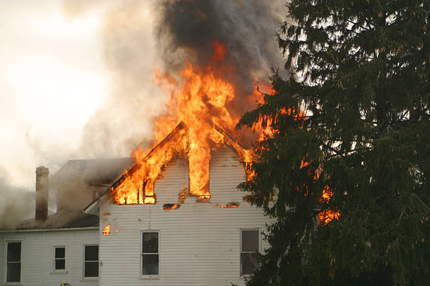 A small house burns to the ground....fireman's hose appears in the foreground