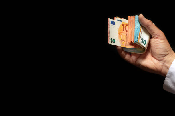 istock Mature man's hand with a folded stack of euro bills on a black background. 1868054264