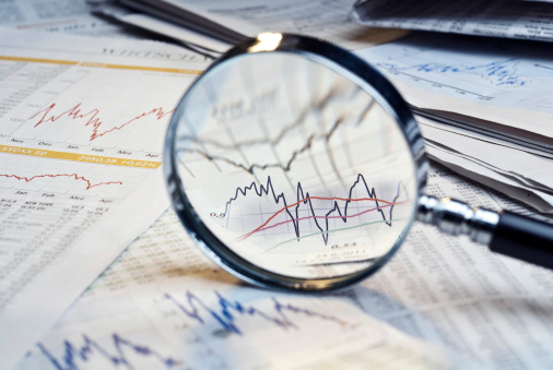 Magnifying glass and newspapers with exchange rate tables and diagrams.