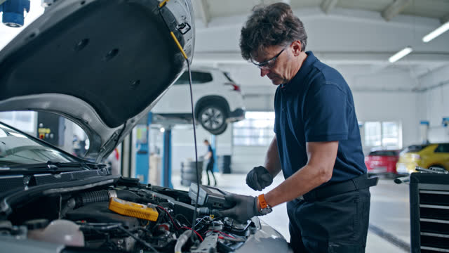 Male mechanic running diagnostic test on car engine in auto repair shop