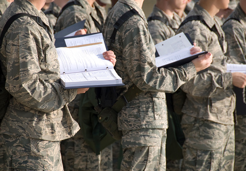 New military men stand with training manuals while attending an outdoor instructional period.