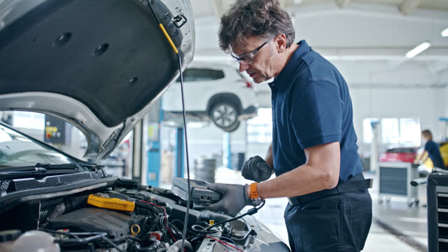 Male mechanic running diagnostic test at car engine in repair shop