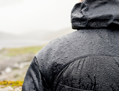 A warm, waterproof jacket protecting a man from heavy rain on a hiking trip.