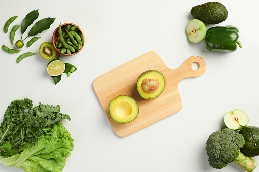 Fresh ripe avocado on cutting board on table with green fruits and veggies