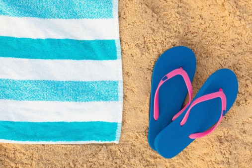Blue and white towel and blue sandals on beach background.