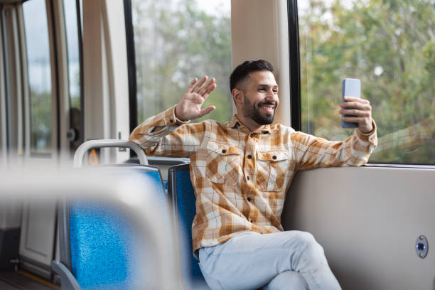 istock handsome latin man makes a video call with his smartphone while riding the train waving 1868111076