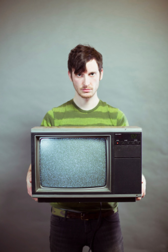 Vertical studio portrait of a sullen young man holding static television. Television is bad concept. ++Toned to create vintage affect.More of this model: