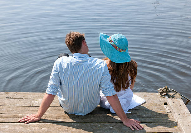 istock young couple sitting on pier at waterfront 186811402