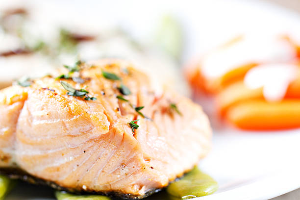 A chef holding a plate full of cooked salmon and vegetables.