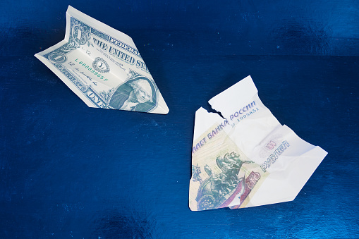 Paper airplane from dollar over paper airplane from hundred rubles bill of Russia on blue background