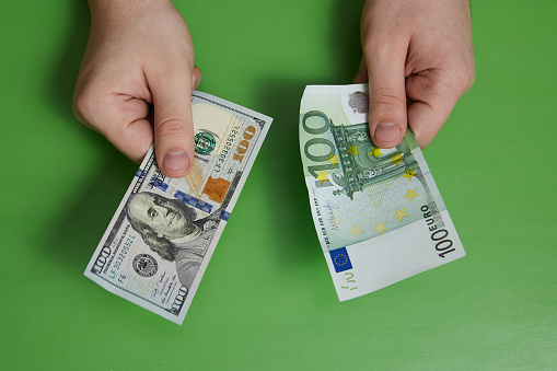 One hundred dollars in one hand and one hundred euros in the other on a green background. Cash currency exchange.