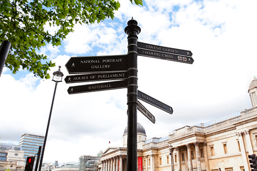 A street sign points to the many famous places that can be found in the Trafalgar Square area. The building in the background is the National Gallery. Points of interest are Covent Garden, Charing Cross, National Gallery, Buckingham Palace, National Portrait Gallery, Houses of Parliament and Whitehall.