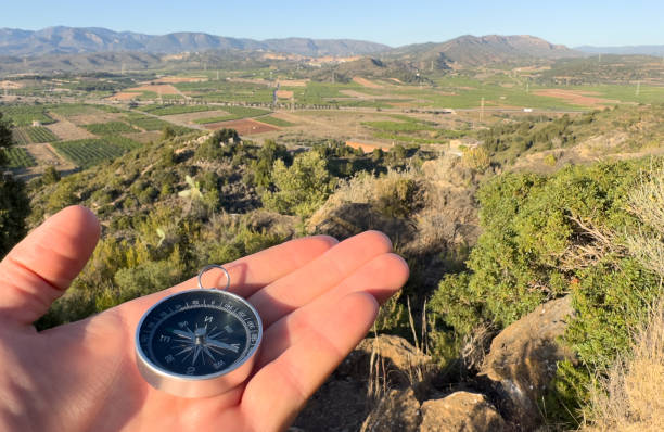 Compass in hand in mountains. Tourist compass for orientation on terrain. Magnetic declination alculator. Map reading and land navigation concept. Orient on maps in mountains