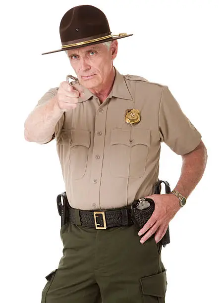 Portrait of a mature male law enforcement officer (highway patrol, sheriff, or park ranger) pointing at the viewer. Isolated on a pure white background.