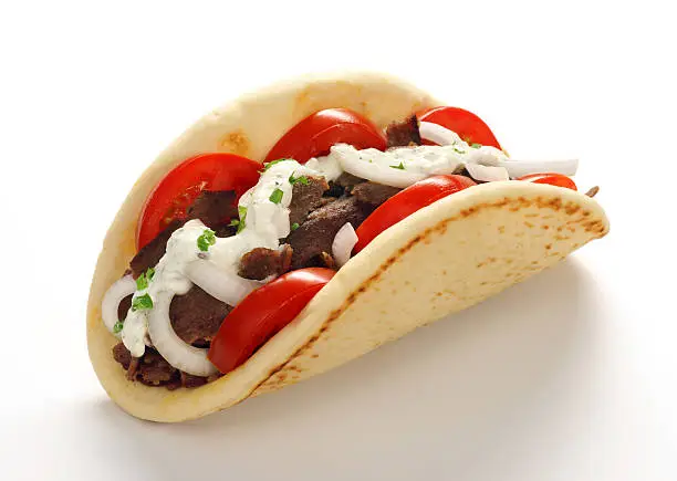 High-resolution digital capture of a freshly prepared Gyros or Doner Kebab; with shaved meat, tomatoes, onions, chives and tzatziki sauce, on fresh pita. Shot on a clean white background with a soft and subtle shadow.