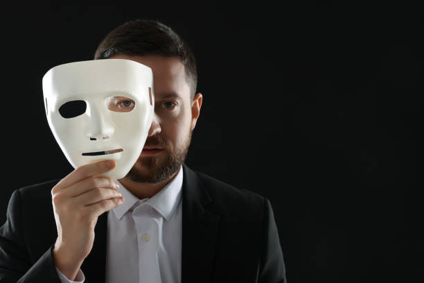 istock Multiple personality concept. Man covering face with mask on black background. Space for text 1868174374