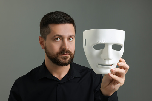 Multiple personality concept. Man with mask on grey background