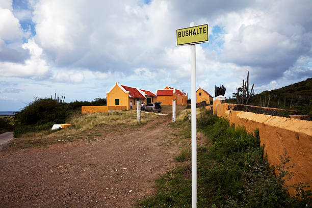 Remote village bus stop, Curacao "A village bus stop, or bushalte, in Kenepa, Curacao. Behind are farmhouse buildings in traditional colonial style, and large cactii, typical of the region, grow nearby." driveway colonial style house residential structure stock pictures, royalty-free photos & images