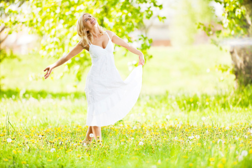 Smiling young woman standing in the field surrounded by lush greenery.  She is looking up.