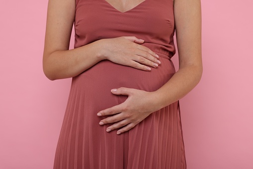 Pregnant woman in dress on pink background, closeup