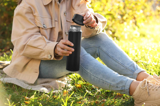 istock Woman opening thermos on green grass outdoors, closeup 1868184302