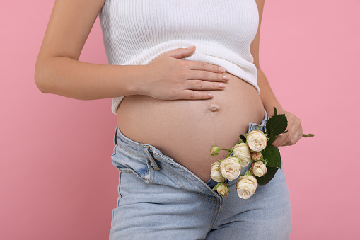 Pregnant woman with roses on pink background, closeup
