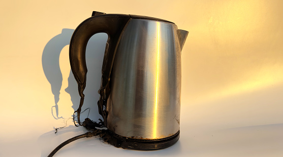 Burning Electric kettle. Electric kettle for tea caught on fire over table. Electric kettle melted due to a short circuit in electrical wiring. Overloaded electrical current or short in device