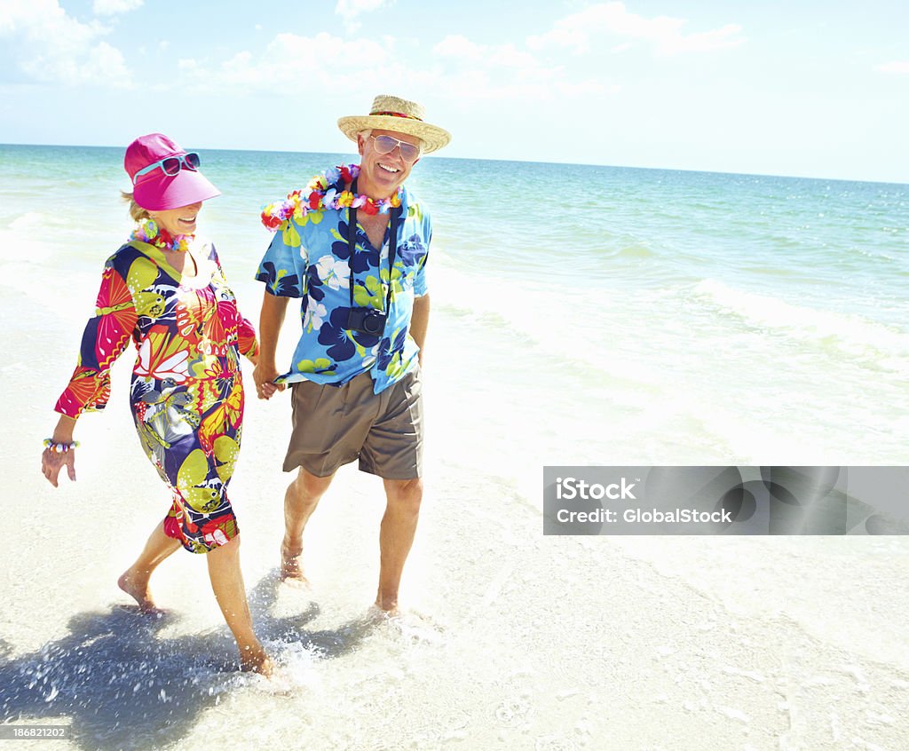 Pensione coppia holding mani lungo la spiaggia - Foto stock royalty-free di 60-69 anni