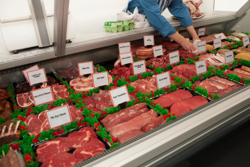 A butcher puts together an order from a selection of fresh raw meats in a large refrigerated counter.