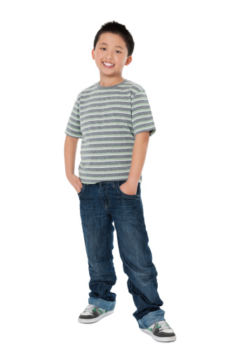 Full length of Chinese little boy smiling with hands in pockets over white background. Vertical Shot.