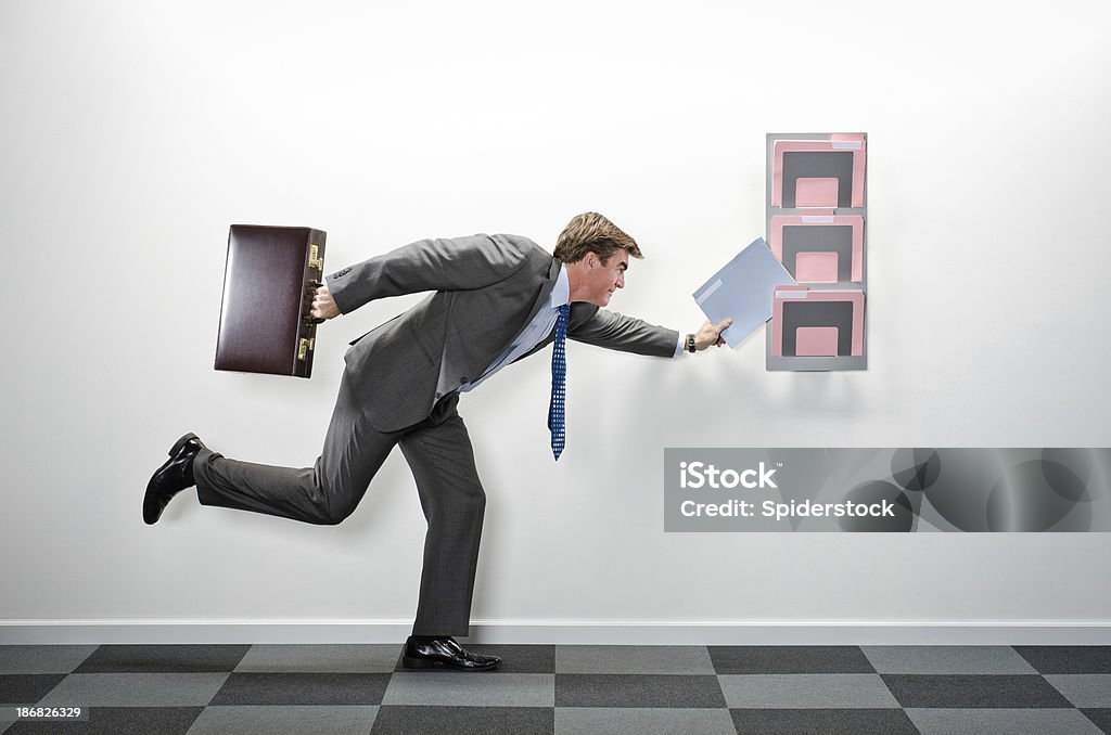 Corporate Executive On The Go "On the go corporate executive with briefcase, filing a folder. The austere room has hanging file folders and checkered felt carpeting.Take a look at our lightbox's of other related images." 40-44 Years Stock Photo