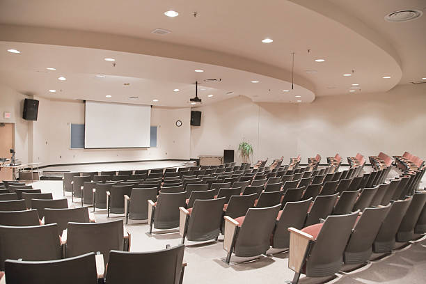 empty lecture hall with several rows of seats and a screen - theaterzaal stockfoto's en -beelden