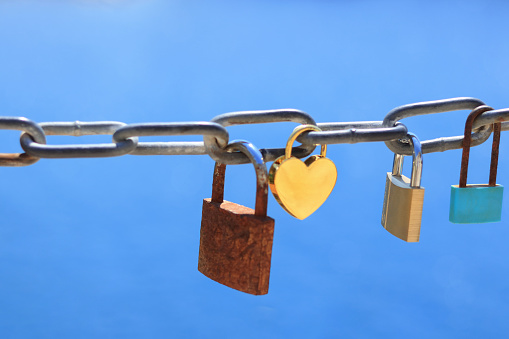 Old rusty love locks on chain against background of blue sea on sunny day. Trip for valentines day Old yellow heart shaped lock. Love lock on the bridge.