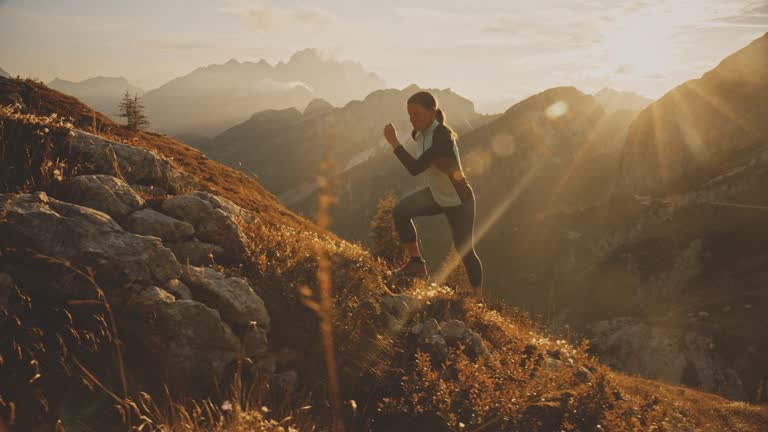 Woman jogging uphill in sunny,majestic mountains at sunrise