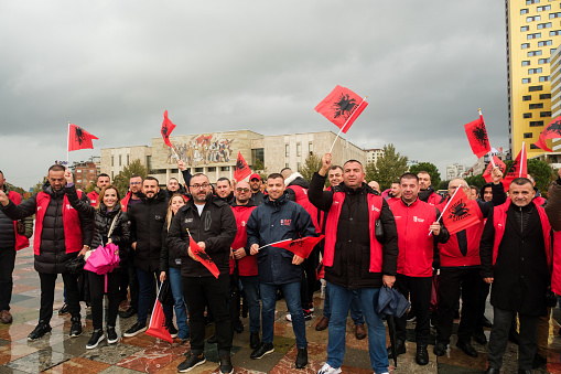 Tirana, Albania - November 28, 2023: In Skanderbeg Square on a rainy Independence Day, we see the crowd enthusiastically participating in the celebrations, holding Albanian flags, with the National History Museum of Tirana in the background