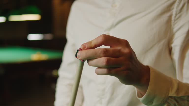 Young billiard player man wearing white shirt preparing a cue for a game close-up. Billiards team sport.