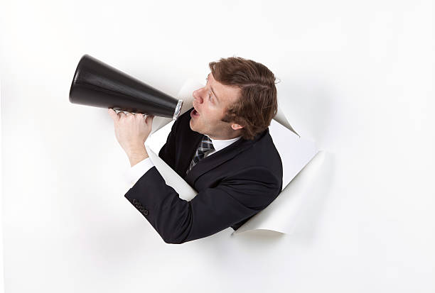 uomo d'affari emergenti attraverso il foro nella carta urlando nel megafono - human mouth paper screaming hole foto e immagini stock